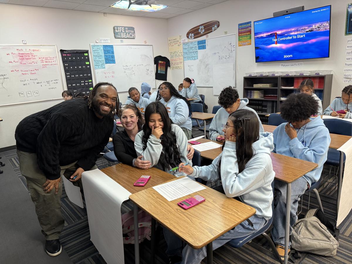 A group of students and a teacher smiling together in a classroom setting.